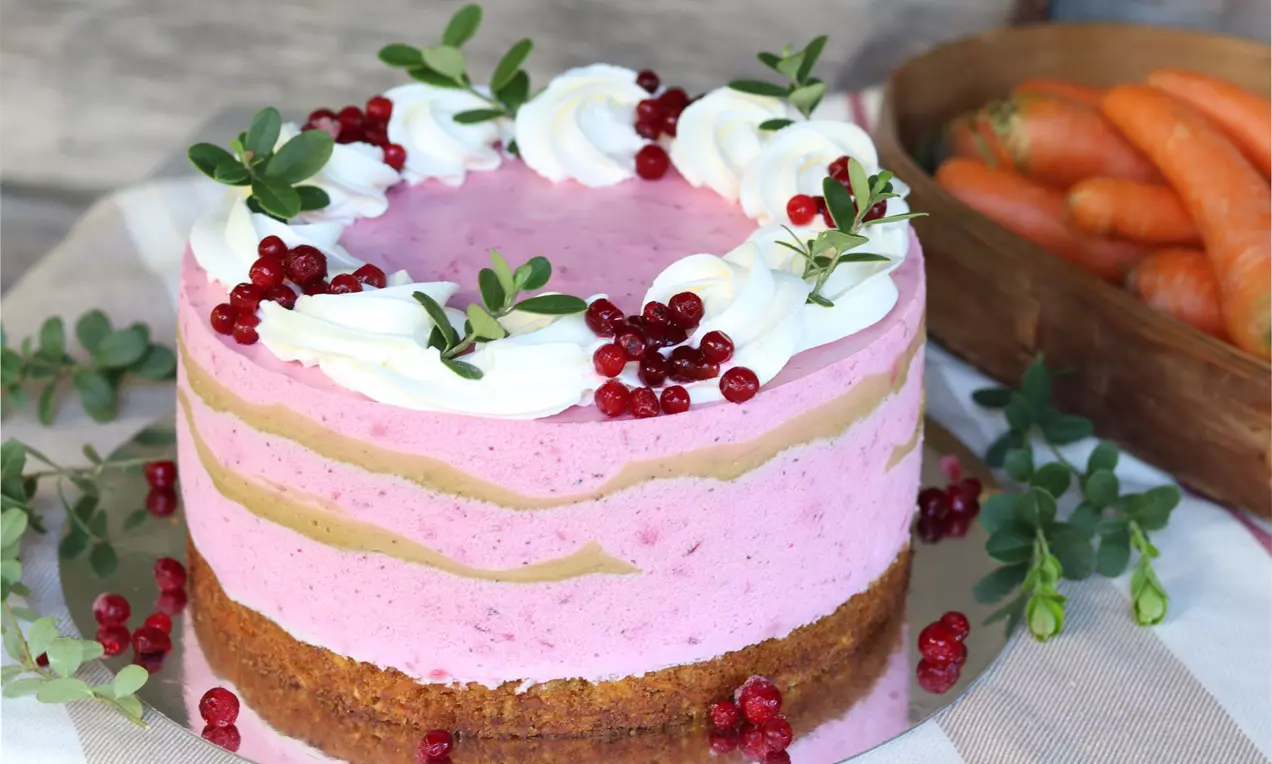 Tyttebær cheesecake med lyserødt fyld og lys bund, pyntet med flødeskumsspiraler, friske tyttebær og grønne blade på lys dug