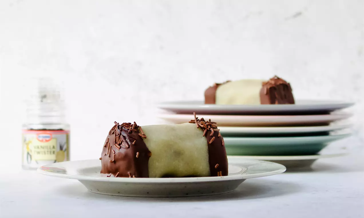 Veganske træstammer med lysegrønt marcipan og glat, mørk chokolade, pyntet med chokoladeflager på lyse tallerkener mod lys baggrund